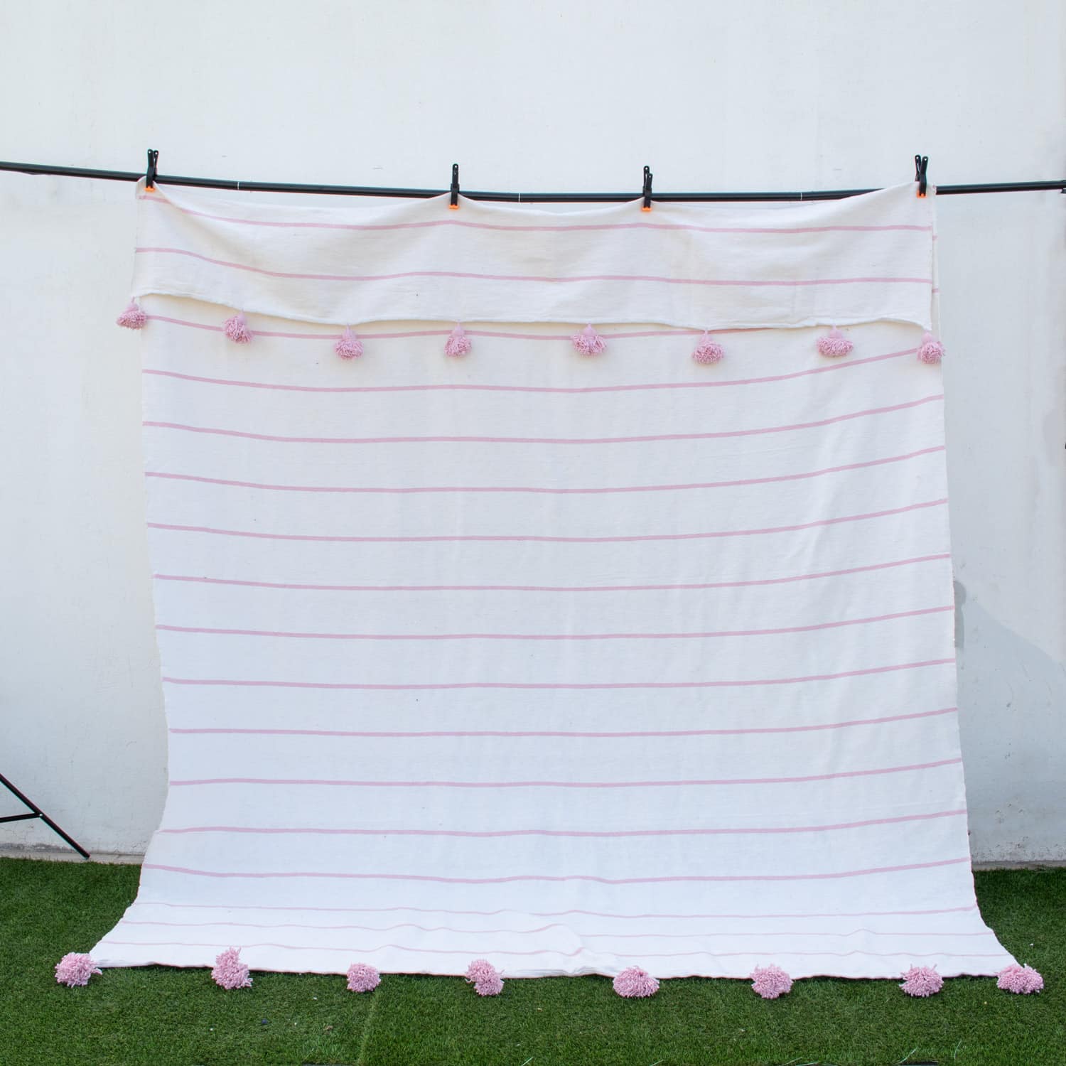 Manta blanca con lineas y pompones rosadas