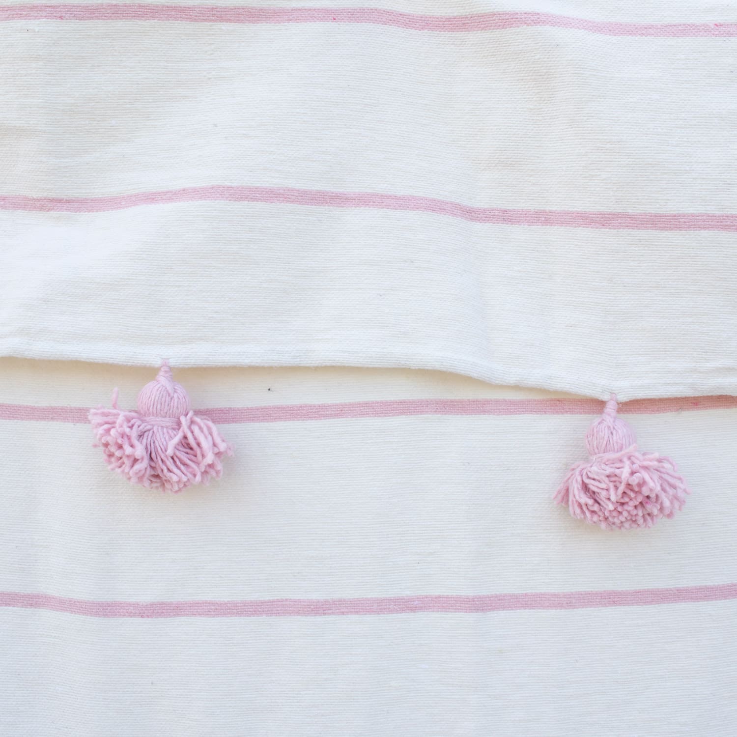 Manta blanca con lineas y pompones rosadas
