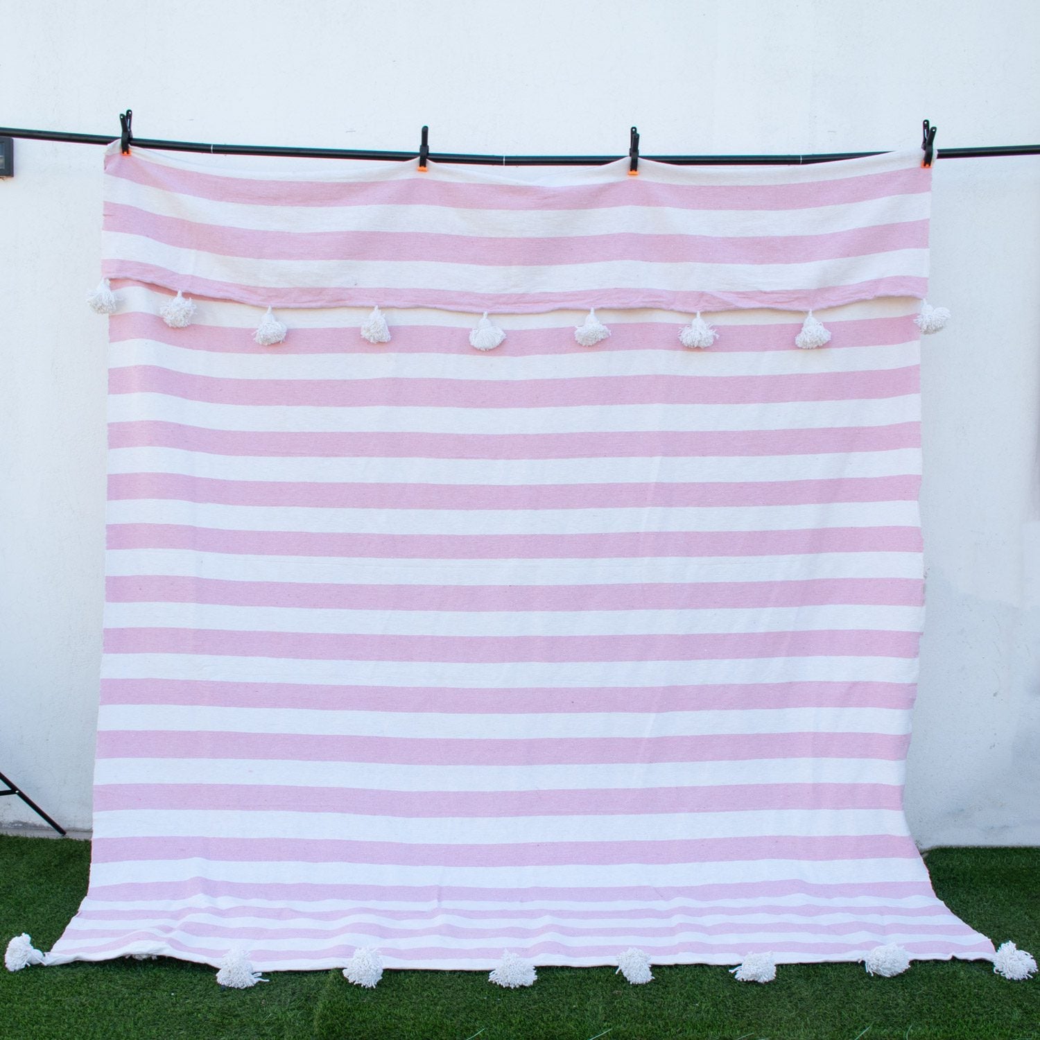 Manta blanca con lineas rosadas y pompones blancos