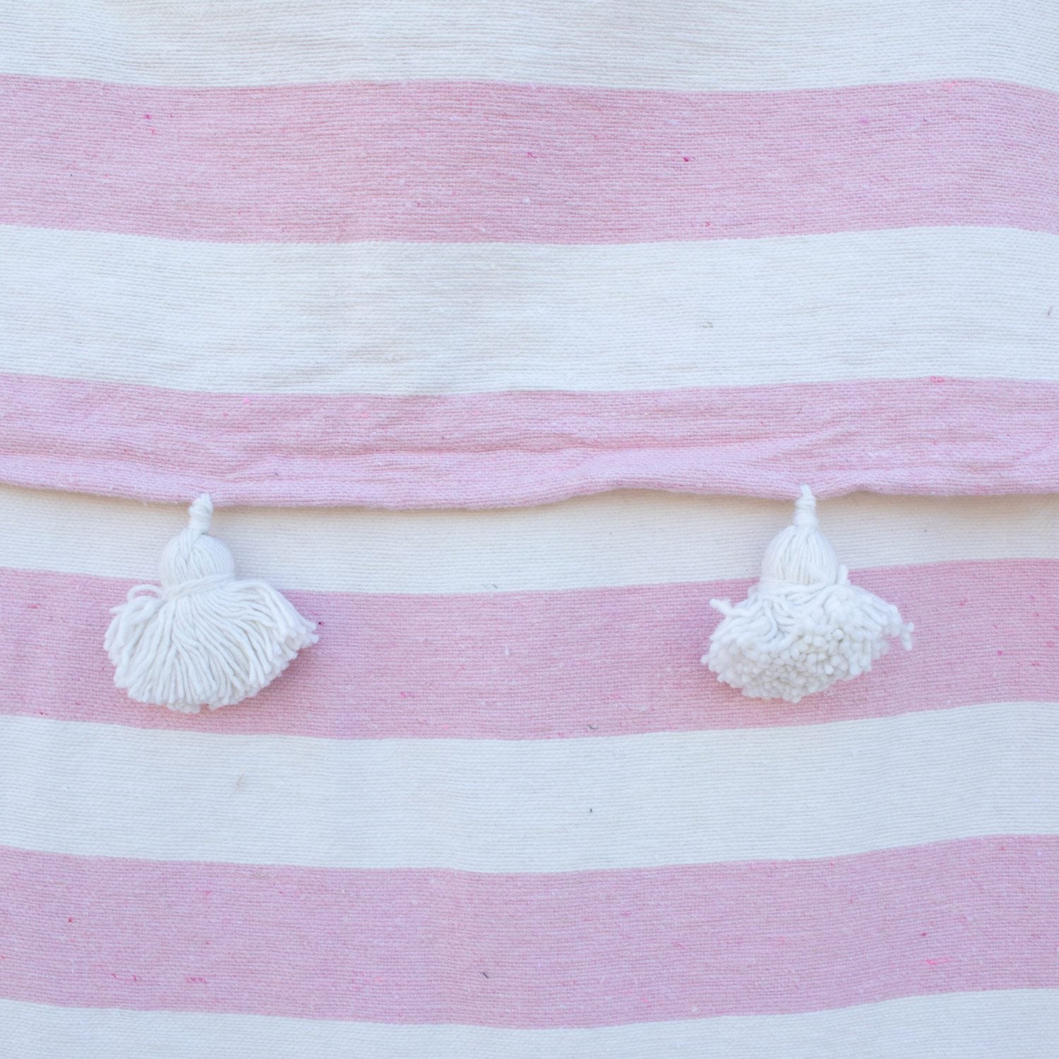 Manta blanca con lineas rosadas y pompones blancos
