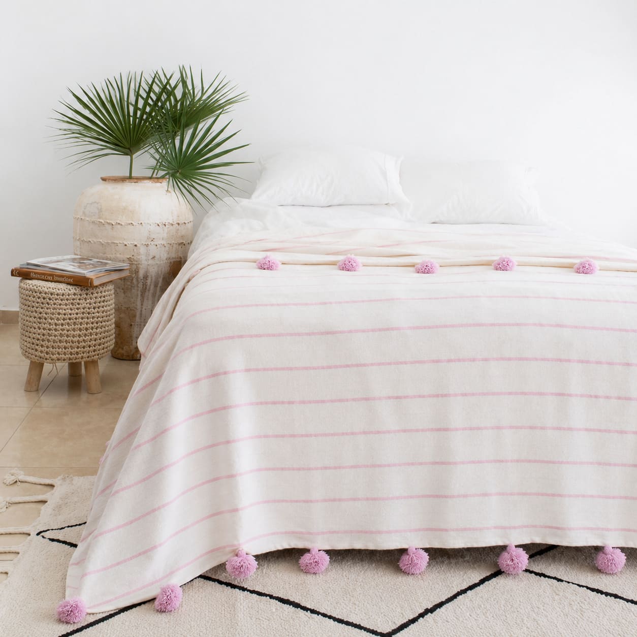 Manta blanca con lineas y pompones rosadas